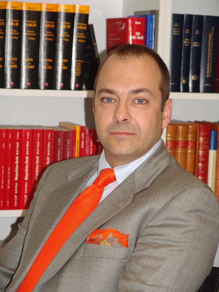 Dr. Giangiacomo Bortoluzzi persönlich, elegant gekleidet mit hellbraunem Sakko, weissem Hemd, orangener Krawatte und Stecktuch.